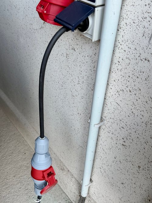 Mitgelieferter Adapter steckt in einer blauen Schuko-Außensteckdose, unten sitzt der CEE-Stecker der Ladestation in der roten Kupplung des Adapters