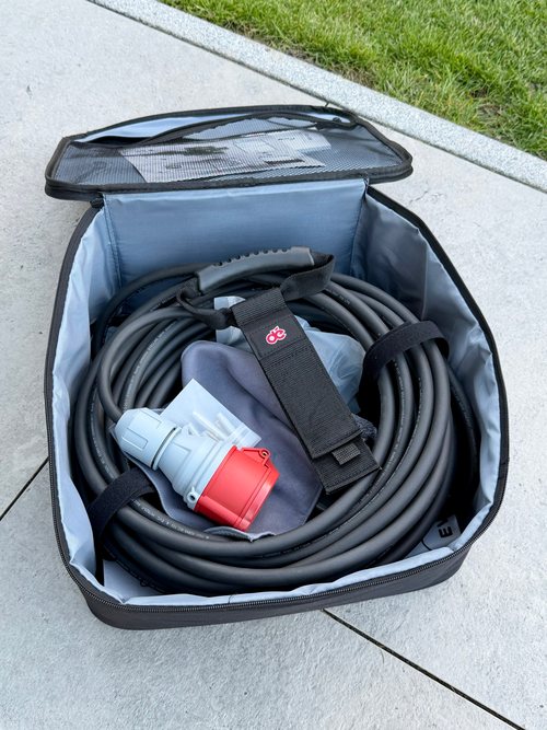 Geöffnete Tragetasche mit aufgerolltem 20-Meter-Ladekabel, Kabelgriff mit Klettband, CEE-Stecker und Schnellstartkarte im Netzfach des Deckels
