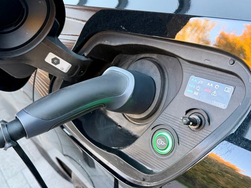 Typ-2-Stecker der dé Mobile Ladestation in der Ladebuchse eines schwarzen Elektroautos, daneben eine grün leuchtende Taste