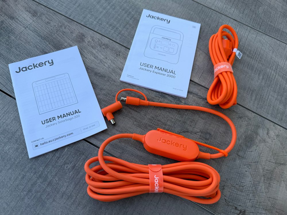Zwei Bedienungsanleitungen, ein oranges AC-Ladekabel und das orange Solar-Anschlusskabel mit kleiner Box und Winkelstecker auf einem Holztisch