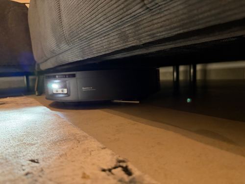 Saugroboter unter dem Sofa im Halbdunkel, vorn leuchtet das Licht am Kameramodul