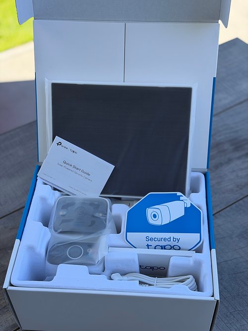 Geöffneter Karton des Tapo C675D KIT mit Solarpanel, Kurzanleitung, Kamera in Schutzfolie und Warnaufkleber Secured by Tapo