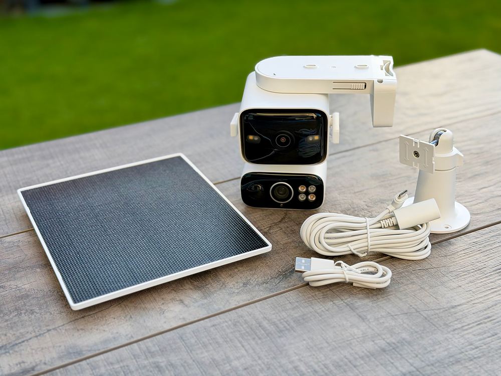 Lieferumfang des Tapo C675D KIT auf einem Gartentisch: Dual-Objektiv-Kamera mit Montagebügel, Solarpanel, Panel-Halterung, Verlängerungskabel und USB-Ladekabel